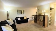 Located at 1699 Shanley Dr in Columbus, Ohio, this single-floor residence offers a straightforward and practical layout designed for comfortable everyday living. The living area serves as the heart of the home, featuring wall-to-wall carpeting that adds warmth underfoot and a neutral color palette that creates a bright, open atmosphere. The space is generously proportioned, providing ample room for seating arrangements and additional furniture pieces such as shelving and accent tables. Natural light filters into the room, complementing the light-toned walls and contributing to an airy feel. A decorative framed mirror adorns one wall, enhancing the sense of space. The room transitions smoothly into an adjacent area, suggesting a connected and functional floor plan well-suited for both relaxing and entertaining. Baseboard heating runs along the perimeter, ensuring comfort throughout the seasons. The overall ambiance of the home is cozy and understated, with clean lines and a neutral aesthetic that offers a versatile canvas for personalization. This Columbus property presents a practical and welcoming living environment in an established neighborhood.