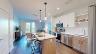 Located on Payne Street in Dover, NH, this modern 2-bedroom, 3-bathroom residence offers a thoughtfully designed single-floor layout with clean contemporary finishes throughout. The open-concept kitchen and living area serves as the heart of the home, where the kitchen stands out with its two-tone cabinetry — white upper cabinets paired with warm natural wood lowers — complemented by white quartz countertops, a subway tile backsplash, and a full suite of stainless steel appliances. A central island with pendant lighting provides additional prep space and casual seating. The adjoining living room is bright and welcoming, with hardwood-style flooring and a glass door leading to an outdoor balcony with open views. The primary bedroom is generously sized, featuring carpet flooring, large windows with outdoor views, and access to its own well-appointed bathroom. A second bedroom offers a comfortable retreat with soft carpet and clean white walls. Both secondary bathrooms feature warm wood vanities, white quartz counters, large mirrors, and hardwood-style flooring. Two dedicated closets, including a spacious walk-in with built-in shelving, provide ample storage. The overall aesthetic is modern, light-filled, and move-in ready.