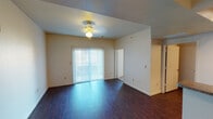 This single-story unit is designed with a practical and cohesive layout that connects the main living areas seamlessly. The living room serves as the central gathering space, finished with rich, dark hardwood-style flooring that extends throughout the main areas. A ceiling fan with light fixture provides overhead illumination, while a full-width sliding glass door dressed with vertical blinds fills the room with natural light and provides outdoor access. The textured ceiling adds subtle architectural character throughout.

The entry foyer offers a welcoming transition into the unit, highlighted by track lighting overhead and a half-wall that separates it from the adjacent kitchen. The kitchen is well-equipped with warm-toned wood cabinetry both above and below granite-style countertops, a double stainless steel sink, and white appliances including a refrigerator, electric range, and built-in microwave. Track lighting illuminates the workspace efficiently.

The bedroom features plush carpeting, a ceiling fan, and a spacious walk-in closet with built-in shelving and hanging rods. The full bathroom includes a wood vanity with granite-style countertop, a large mirror, a shower-tub combination, and matching hardwood-style flooring, completing the unit's consistent design aesthetic.