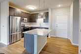Located at 667 S Whitney Way in Madison, WI, this well-designed 2-bedroom, 1-bathroom unit offers a thoughtful layout across a single floor. The open-concept kitchen and living area serves as the heart of the home, anchored by a central island with striking granite countertops and illuminated by sleek pendant lighting. The kitchen is equipped with stainless steel appliances, dark espresso cabinetry, a white subway tile backsplash, and ample storage. Light hardwood flooring flows throughout, enhancing the bright, contemporary feel. Sliding glass doors in the living area open to a private balcony, inviting natural light and outdoor views. The primary bedroom is a comfortable, well-proportioned retreat, while the second bedroom features a large window overlooking the exterior. The shared bathroom continues the upscale finishes seen throughout, showcasing a granite-topped vanity, dark wood cabinetry with built-in storage tower, and a large mirror. Three closets provide generous storage, and an in-unit laundry area adds everyday convenience. Neutral tones and modern finishes create a cohesive, move-in-ready aesthetic throughout the entire space.