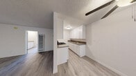 This single-floor unit offers a clean, functional layout with consistent light wood-tone flooring throughout, creating a cohesive and inviting atmosphere. The galley-style kitchen is well-equipped, featuring crisp white shaker cabinetry, dark granite-style countertops, a gas range with overhead ventilation, and a double-basin stainless steel sink. Ample upper and lower cabinet storage lines both sides of the kitchen, maximizing utility in the space. A partial wall divides the kitchen from the adjacent living area, providing a sense of separation while maintaining an open feel. The living area is spacious and bright, with neutral white walls and a textured ceiling that adds subtle character. Natural light filters in through windows fitted with vertical blinds. A wall-mounted heating unit serves the living space, and a doorway leads to the bedroom beyond. The bedroom is generously sized, offering a clean, open layout with its own window for natural light. The bathroom features a granite-style vanity countertop with a round undermount sink, white cabinetry below, and a large mirror above. The shower/tub combo is bright and clean, with a window above providing natural ventilation and light. Throughout the unit, light-toned wood-style flooring and neutral walls create a fresh, move-in-ready environment.