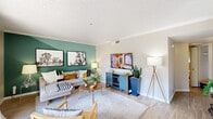 This thoughtfully designed single-floor residence offers a seamless blend of modern aesthetics and functional living. The living room serves as the heart of the home, highlighted by a bold green accent wall, light wood-style flooring, crown molding, and a textured ceiling. Large sliding glass doors flood the space with natural light and open directly onto a private balcony overlooking a landscaped exterior. The adjacent dining area accommodates a round glass-top table beneath a sleek ceiling fan, with a window providing additional natural light. A passthrough connects the dining space to the galley-style kitchen, which features rich dark wood cabinetry, light quartz countertops, a mosaic tile backsplash, stainless steel appliances, and a deep undermount sink. The two bedrooms are comfortably sized, each equipped with ceiling fans, windows with sheer curtains and blinds, and neutral wall tones that create a calm, restful atmosphere. The bathroom is clean and well-finished, featuring a framed vanity mirror, modern light fixture, wood-toned cabinetry, and a shower-tub combination. Light wood-style flooring flows consistently throughout the residence, enhancing the cohesive, contemporary feel of the entire space.
