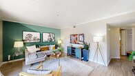 This thoughtfully designed single-floor residence offers a seamless blend of modern aesthetics and functional living. The living room serves as the heart of the home, highlighted by a bold green accent wall, light wood-style flooring, crown molding, and a textured ceiling. Large sliding glass doors flood the space with natural light and open directly onto a private balcony overlooking a landscaped exterior. The adjacent dining area accommodates a round glass-top table beneath a sleek ceiling fan, with a window providing additional natural light. A passthrough connects the dining space to the galley-style kitchen, which features rich dark wood cabinetry, light quartz countertops, a mosaic tile backsplash, stainless steel appliances, and a deep undermount sink. The two bedrooms are comfortably sized, each equipped with ceiling fans, windows with sheer curtains and blinds, and neutral wall tones that create a calm, restful atmosphere. The bathroom is clean and well-finished, featuring a framed vanity mirror, modern light fixture, wood-toned cabinetry, and a shower-tub combination. Light wood-style flooring flows consistently throughout the residence, enhancing the cohesive, contemporary feel of the entire space.