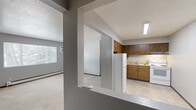 Located at 285 Robins Rd in Hiawatha, Iowa, this two-bedroom, one-bathroom residence offers a practical single-floor layout designed for comfortable everyday living. The living room is a bright, open space featuring large windows that invite natural light and offer views of the surrounding greenery, complemented by neutral-toned carpet and a textured ceiling. Baseboard heating runs throughout the unit, providing consistent warmth. The kitchen is efficiently laid out with warm wood-toned cabinetry, light countertops, tile flooring, and white appliances including a refrigerator, electric range, and overhead ventilation — all illuminated by a flush-mounted fluorescent light. A hallway connects the main living areas to the bedrooms and bathroom. The primary bedroom is generously sized, featuring a ceiling fan, a large window with outdoor views, and ample closet space with sliding wood-paneled doors. The second bedroom also includes a window, ceiling fan, and carpet flooring. The bathroom is equipped with a full tub-shower combination with chrome fixtures. Three closets throughout the unit provide excellent storage. The overall aesthetic is clean and functional, with consistent gray walls, wood trim, and carpeted bedrooms throughout.