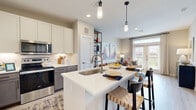Located at 20130 Schiel Rd in Cypress, TX, this single-story residence offers a thoughtfully designed open-concept layout that seamlessly connects the kitchen, dining, and living areas. The kitchen is a standout feature, showcasing white upper cabinetry paired with two-tone lower cabinets, light wood-style flooring, a large center island with a quartz countertop and built-in sink, and a full suite of stainless steel appliances including a refrigerator, range, and over-the-range microwave. Pendant lighting above the island adds a modern touch, while recessed lighting illuminates the entire space. The living area flows naturally from the kitchen, bathed in natural light from large windows and a glass door that opens to an outdoor area with open views. The bedrooms offer plush carpeting, ceiling fans, and generous windows that bring in ample daylight and exterior views. The primary bathroom is elegantly finished with light tile flooring, a quartz-topped vanity, and convenient access to a spacious walk-in closet complete with built-in shelving and hanging rods. A stacked in-unit washer and dryer is also accessible from the bathroom area. Throughout the residence, a neutral color palette and contemporary finishes create a clean, cohesive, and inviting atmosphere.