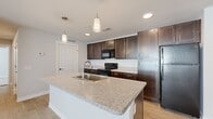 This single-floor, 2-bedroom, 1-bathroom residence offers a practical and modern layout designed for comfortable living. The open-concept kitchen and living area serves as the heart of the home, featuring light wood-look flooring that runs throughout the main space. The kitchen is well-equipped with dark espresso cabinetry, black appliances including a refrigerator and range, and a generous kitchen island topped with speckled granite countertops. Pendant lighting above the island adds a stylish touch, while recessed ceiling lights provide ample illumination throughout.

The living area is bright and airy, benefiting from natural light and a ceiling fan overhead. The two bedrooms offer a calm retreat, each carpeted for comfort and featuring windows with blinds that allow for natural light control. The primary bedroom is a well-proportioned space, and both rooms are served by four closets throughout the unit, including a walk-in closet with wire shelving for organized storage.

The full bathroom is finished with wood-look tile flooring, a dark-cabinet vanity with a white countertop, and a full tub-shower combination. Neutral, light-toned walls throughout the entire residence create a clean, cohesive aesthetic that is both inviting and versatile.