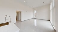 Located at 78 Middlesex St in Lowell, MA, this one-bedroom, one-bathroom unit offers a clean, modern aesthetic throughout its single-floor layout. The space is defined by a consistent use of polished terrazzo flooring that runs throughout, crisp white walls, and an abundance of natural light streaming in through large windows that frame views of the surrounding urban streetscape.

The open kitchen is a standout feature, equipped with white shaker cabinetry, stainless steel appliances including a range, microwave, and refrigerator, and a white countertop island with a deep undermount sink and a sleek pull-down faucet. Generous floor-to-ceiling windows adjacent to the kitchen flood the space with natural light and provide lively city views.

The living area is bright and open with notably high ceilings and recessed lighting, creating an airy, spacious feel. A hallway connects to the private bedroom, which features a large window overlooking the neighborhood and offers a cozy, well-proportioned retreat.

The bathroom is finished in the same minimalist style, featuring a soaking tub with shower, a wall-mounted floating vanity with a vessel sink, a backlit mirror, and terrazzo flooring, all in a clean, all-white palette that reinforces the unit's modern sensibility throughout.