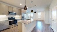 This well-designed 3-bedroom, 2-bathroom residence in Austin, TX offers a thoughtfully laid-out single-floor plan with modern finishes throughout. The open-concept kitchen and living area serves as the heart of the home, anchored by a large granite-topped island with a built-in sink and stylish pendant lighting. The kitchen features stainless steel appliances, taupe cabinetry, a classic subway tile backsplash, and ample counter space. Wood-look flooring flows seamlessly through the main living areas, while natural light pours in through multiple windows, including a sliding door that opens to an outdoor balcony. The primary bedroom is a generously sized retreat with a ceiling fan, carpet flooring, and a private en-suite bathroom. The en-suite features granite countertops, dual sinks, white cabinetry, and direct access to a walk-in closet with built-in shelving. The two additional bedrooms are well-proportioned, each with carpet flooring, ceiling fans, and natural light from large windows. A notable feature of this home is its six closets, providing exceptional storage throughout. The overall aesthetic is clean and contemporary, with a bright, neutral palette that creates a welcoming and versatile living environment.