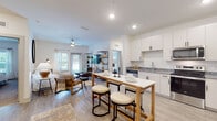 Located at 6322 Race Track Rd in Saint Johns, FL, this thoughtfully designed single-floor residence offers a bright, open-concept layout that seamlessly connects the kitchen, dining, and living areas. The kitchen is a standout feature, equipped with stainless steel appliances — including a side-by-side refrigerator, range, and over-the-range microwave — complemented by granite countertops, crisp white cabinetry with black hardware, and light wood-look flooring. A kitchen island with bar seating provides an ideal casual dining space. The open living area is bathed in natural light from multiple windows and features a ceiling fan, creating an airy and welcoming atmosphere. The primary bedroom is generously sized with large windows, plush carpeting, and access to a well-appointed en-suite bathroom. The bathroom offers a dual-sink vanity with granite countertops, a walk-in glass-enclosed shower, and wood-look flooring. A spacious walk-in closet serves the primary suite. A second bedroom provides comfortable accommodations, also carpeted and filled with natural light. The dedicated laundry room houses a full-size washer and dryer with overhead shelving for added convenience. Clean white walls and consistent finishes throughout lend a cohesive, modern aesthetic to the entire residence.