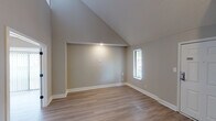 This two-story residence at 7835 N Point Blvd in Winston-Salem, North Carolina, offers a well-designed layout that maximizes vertical space and natural light throughout. The main level features a welcoming entryway with light wood-tone flooring that flows through the open living areas. The kitchen is outfitted with white shaker-style cabinetry, granite-look countertops, a stainless steel appliance suite including a refrigerator, range, microwave, and dishwasher, and a built-in butcher block island that adds functional workspace. A bright living room on the main floor benefits from vertical blinds and vaulted ceiling elements that create an airy, open feel. The carpeted staircase with a white balustrade leads to the upper level, where dramatic vaulted ceilings rise to impressive heights, particularly notable in the upper-level room with its tall angled roofline and a narrow window that draws in natural light. Two full bathrooms serve the home: one features a tub-shower combination with tile surround, a warm granite-topped vanity, and white cabinetry, while the other offers a dual-sink vanity with ample storage. Throughout the home, neutral warm-gray tones, clean white trim, and consistent wood-look flooring create a cohesive and move-in-ready aesthetic.