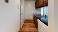 Located at 171 Hartford Rd in the Fairway neighborhood of New Britain, CT, this single-floor residence offers a well-organized layout designed for comfortable everyday living. The spacious living room is a standout feature, showcasing plush wall-to-wall carpeting, baseboard heating, and an abundance of natural light streaming in through large windows and a full-width sliding glass door that opens to a private balcony with treetop views. The open feel of the living area is enhanced by a pass-through window connecting it to the kitchen, creating a cohesive and sociable layout. The galley-style kitchen is efficiently designed, featuring warm wood cabinetry, dark countertops, white tile backsplash, hardwood flooring, and a full suite of appliances including a refrigerator, electric range, dishwasher, and double sink. The bathroom is clean and functional, appointed with hardwood flooring, a full tub and shower combination, a toilet, and a white vanity with cabinet storage. Throughout the unit, the interplay of light-toned walls, natural wood finishes, and generous window placement creates a bright, welcoming ambiance well-suited to a variety of lifestyles.