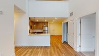 This two-story residence showcases a striking architectural design highlighted by dramatic double-height ceilings in the main living area, which flood the space with natural light through tall windows and sliding glass doors. The ground floor centers around an open-concept layout where the living area flows seamlessly into a well-appointed kitchen featuring warm wood cabinetry, granite countertops, a breakfast bar peninsula with pendant lighting, and a full suite of stainless steel appliances. A second, separate kitchen is also present, outfitted with contemporary light wood cabinetry, matching stainless steel appliances, and clean subway tile backsplash — offering exceptional flexibility. Light hardwood flooring runs throughout the main level, contributing to the bright, airy atmosphere. The upper floor features a loft-style landing that overlooks the living area below, reinforcing the home's sense of openness and vertical scale. Bedrooms are carpeted for comfort and bathed in natural light through windows with blinds, while a spacious walk-in closet provides generous storage. The bathroom is finished with granite countertops, tile flooring, and a full tub-shower combination. Throughout both floors, the clean white walls and recessed lighting create a cohesive, modern ambiance.
