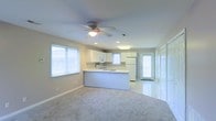 This two-floor home offers a clean, welcoming atmosphere defined by its light-filled interiors and thoughtfully designed layout. The main living area is open-concept, seamlessly connecting the living room and kitchen in a spacious, cohesive flow. Plush carpeting anchors the living space, while tile flooring transitions into the kitchen and entry areas, creating a natural delineation between zones.

The kitchen is a standout feature, highlighted by white cabinetry, a functional peninsula that provides additional counter and prep space, and a suite of appliances including a refrigerator and range. A large window above the sink invites natural light, complementing the recessed lighting and overhead fixtures throughout. The kitchen also benefits from direct access to an exterior door, adding convenience and connectivity to the outdoors.

A ceiling fan with a built-in light fixture is centrally positioned in the living area, enhancing both comfort and illumination. Multiple windows fitted with blinds allow for adjustable natural light across the main floor. The neutral color palette of soft whites and warm grays lends the entire space a calm, versatile ambiance, making it easy to personalize. The two-floor layout provides additional living space beyond the open main level.