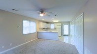 This two-floor home offers a clean, welcoming atmosphere defined by its light-filled interiors and thoughtfully designed layout. The main living area is open-concept, seamlessly connecting the living room and kitchen in a spacious, cohesive flow. Plush carpeting anchors the living space, while tile flooring transitions into the kitchen and entry areas, creating a natural delineation between zones.

The kitchen is a standout feature, highlighted by white cabinetry, a functional peninsula that provides additional counter and prep space, and a suite of appliances including a refrigerator and range. A large window above the sink invites natural light, complementing the recessed lighting and overhead fixtures throughout. The kitchen also benefits from direct access to an exterior door, adding convenience and connectivity to the outdoors.

A ceiling fan with a built-in light fixture is centrally positioned in the living area, enhancing both comfort and illumination. Multiple windows fitted with blinds allow for adjustable natural light across the main floor. The neutral color palette of soft whites and warm grays lends the entire space a calm, versatile ambiance, making it easy to personalize. The two-floor layout provides additional living space beyond the open main level.