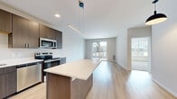 Located at 8421 Mansion Hill Ave in Madison, WI, this well-appointed one-bedroom, one-bathroom unit offers a thoughtfully designed single-floor layout. The open-concept kitchen and living area serves as the heart of the space, featuring light hardwood-style flooring that enhances the bright, airy atmosphere. The modern kitchen is equipped with full stainless steel appliances — including a refrigerator, range, microwave, and dishwasher — complemented by rich dark wood cabinetry, white quartz countertops, a central island with pendant lighting, and a sleek undermount sink. The living area extends naturally from the kitchen and opens to a private outdoor balcony through sliding glass doors, inviting natural light and neighborhood views. The bedroom is a comfortable retreat finished with plush carpeting, a ceiling fan, and a large picture window that frames views of the surrounding community. A dedicated closet provides convenient storage. The bathroom is finished with contemporary light wood cabinetry, a wide vanity with an illuminated mirror, and an in-unit stacked washer and dryer — adding a practical, modern touch. Neutral tones, clean lines, and quality finishes throughout create a cohesive and inviting living environment.