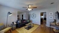 This single-story, 3-bedroom, 2-bathroom home offers a well-organized layout designed for comfortable everyday living. The living room serves as the heart of the home, featuring warm hardwood-style flooring, a ceiling fan with light fixture, and a textured ceiling that adds character to the space. A built-in shelving unit with mirrored backing provides both storage and a sense of depth, while the open sightline into the kitchen creates a naturally connected and sociable atmosphere. The kitchen is visible from the living area and appears well-appointed with dark cabinetry, ample counter space, and natural light streaming through a window — making it both functional and inviting. The overall color palette throughout the home is neutral and versatile, with light gray walls that complement a variety of décor styles. The floor plan flows efficiently between the living, dining, and kitchen areas, maximizing the use of the available square footage. With three bedrooms, the home offers flexibility for families, guests, or a dedicated home office. Two full bathrooms add convenience and practicality. The single-floor layout ensures easy accessibility throughout, making this home a straightforward and functional living space suited to a wide range of lifestyles.