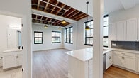 Located at 349 E Main Ave in Zeeland, MI, this 1-bedroom, 1-bathroom unit blends industrial character with modern design. The open-concept living area is a standout, featuring dramatic exposed wood beam ceilings with visible joists, black-framed multi-pane windows that flood the space with natural light, and warm wood-look luxury vinyl plank flooring that runs throughout. Pendant lighting adds a contemporary touch overhead.

The kitchen is well-appointed with white shaker cabinetry, white quartz countertops, a slate-blue subway tile backsplash, stainless steel appliances including a range, microwave, and French door refrigerator, and a central island with additional storage. Large windows above the counters bring in ample daylight and outdoor views.

The bedroom is a calm, light-filled retreat with two large black-framed windows offering street views, neutral walls, and the same consistent flooring. The full bathroom features porcelain tile flooring, a white vanity with quartz top, a tub/shower combination, and clean, minimalist finishes throughout.

A dedicated laundry area includes a stacked washer and dryer unit alongside built-in shelving for added storage. The space is thoughtfully designed to maximize both function and style within its efficient footprint.