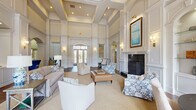 The clubhouse at Avemore Apartment Homes on Avemore Lane in Charlottesville, Virginia, presents a sophisticated, single-story gathering space defined by its grand architectural character and carefully curated interiors. Soaring coffered ceilings draw the eye upward throughout the main lounge, where tall wainscoted walls finished in crisp white millwork establish a refined, traditional aesthetic. Recessed arched doorways with decorative moldings connect the various areas seamlessly, lending a sense of continuity and elegance across the floor plan.

The central lounge serves as the heart of the space, anchored by a stately fireplace clad in dark granite with an ornate white surround and flanked by built-in display niches with glass shelving. Comfortable seating arrangements invite relaxed conversation and socializing. Hardwood flooring grounds the room, while neutral area rugs define each seating zone.

Natural light is a prominent feature, streaming through tall arched windows and distinctive circular clerestory windows that frame views of the outdoor pool and surrounding landscaping. Wall sconces with warm brass hardware complement the ambient recessed lighting throughout. An adjacent office area, accessible through a arched opening, provides a functional workspace. The overall ambiance is polished, welcoming, and reflective of classic Virginia charm.