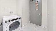 This 60 square foot laundry room, situated in Maple Ridge, British Columbia, exemplifies efficient space utilization. The room features sleek, modern Maytag washing machines, indicating a focus on high-quality appliances. The floor is adorned with a luxurious marble-like material, adding a touch of elegance to the utilitarian space. Crisp white walls create a clean, bright atmosphere, while a gray security door with a small window provides both safety and natural light. The room's design incorporates practical elements such as electrical outlets for convenience. A notable feature is the seamless baseboard that matches the flooring, contributing to a cohesive look. The compact nature of the space is evident, yet it doesn't compromise on functionality. This laundry room demonstrates how even small areas can be transformed into efficient, attractive spaces when designed thoughtfully.