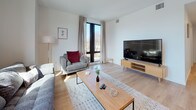 This thoughtfully designed 2-bedroom, 2-bathroom residence features a clean, modern aesthetic across a single floor. The open-concept living and dining area is bathed in natural light through large floor-to-ceiling windows with outdoor views, and is finished with warm light wood flooring that extends into the kitchen. The kitchen is outfitted with sleek white flat-panel cabinetry, white quartz countertops, a stainless steel dishwasher, range, and built-in microwave, creating a polished and functional cooking space. The living area provides ample room for comfortable seating and a dining setup, making it ideal for both relaxing and entertaining. Both bedrooms are carpeted and feature large windows that invite natural light and outdoor views, with the primary bedroom including a sliding frosted-glass closet door. Each bathroom mirrors the modern design language of the home, featuring white floating vanities with undermount sinks, white quartz countertops, large mirrors, and light wood-style flooring. The overall ambiance of the residence is bright, clean, and contemporary, with a neutral color palette and consistent finishes that create a cohesive and inviting living environment throughout.