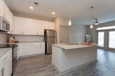 This single-floor residence offers a well-designed layout that balances functionality with modern aesthetics throughout. The kitchen serves as a standout feature, showcasing crisp white shaker cabinetry, granite countertops, and a full suite of stainless steel appliances, including a range, microwave, refrigerator, and dishwasher. A subway tile backsplash adds a clean, classic touch, while a central island with pendant lighting and an undermount sink provides additional workspace and casual seating potential. Wood-look luxury vinyl flooring flows through the kitchen and main living areas, adding warmth and durability.

The bedrooms are finished with plush carpeting and ceiling fans, contributing to a comfortable atmosphere. One bedroom benefits from multiple windows that invite natural light and views of the surrounding neighborhood. A generously sized walk-in closet with wire shelving systems offers practical storage. The bathroom features granite-topped white vanity cabinetry, a wide mirror, wood-look tile flooring, and a tub-shower combination.

A notable highlight is the entryway, framed by full-light French doors with a transom window above, flooding the space with natural light and creating a welcoming, open feel upon arrival.