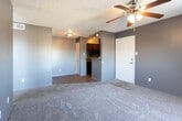 Located at 4900 E University Blvd in Odessa, Texas, this single-floor unit offers a compact, functional layout with a distinctly modern aesthetic defined by deep charcoal and dark gray wall tones throughout. The living area is carpeted and open, featuring a ceiling fan with light fixture and a front entry door that connects directly to the kitchen pass-through. A bold dark accent wall creates a strong visual boundary between the living space and the hallway leading to the bedroom. The bedroom continues the dark color scheme with the same dramatic charcoal accent wall, plush carpet, a ceiling fan, and a closet with sliding doors. Natural light filters in through a window, adding brightness to the otherwise moody interior. The galley-style kitchen is equipped with dark cabinetry, laminate countertops, a single-basin sink, wood-look flooring, and black appliances including a refrigerator and range with overhead ventilation. The bathroom features wood-look flooring, a full-size tub and shower combo with white square tile surround, and dark wall paint that maintains the unit's cohesive design language. Overall, the space presents a bold, contemporary character well-suited for modern living.