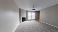 This single-floor residence offers a thoughtfully designed layout with a comfortable and cohesive aesthetic throughout. The spacious living room serves as the heart of the home, featuring plush wall-to-wall carpeting, a tile-surround fireplace, a ceiling fan, and a large sliding glass door fitted with vertical blinds that invites natural light into the space. The open-concept kitchen is accessible via a peninsula-style counter with light stone countertops, complemented by dark-toned cabinetry, stainless steel appliances including a refrigerator and microwave, and wood-look flooring. A dedicated laundry area with built-in shelving is conveniently accessible directly from the kitchen. The bedrooms are generously sized, each finished with soft carpeting, neutral taupe walls, and ample natural light provided by horizontal-blind windows. Ceiling fans are present in multiple rooms for added comfort. The bathrooms feature clean, modern finishes with large-format light gray tile surrounding deep soaking tubs with shower combinations, chrome fixtures, and wood-look tile flooring. The overall ambiance is neutral, move-in ready, and functional, with a consistent warm-gray color palette tying the entire space together.