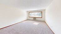 Located at 1701 E 80th St in Bloomington, MN, this single-floor, 2-bedroom, 1-bathroom unit offers a practical and comfortable layout. The living area features neutral-toned carpet, warm wood baseboards, and a ceiling fan, creating a bright and functional space. An open transition connects the living area to the kitchen, which includes wood cabinetry and a range, providing a straightforward and efficient workspace. The generously sized primary bedroom is a standout feature of this unit, offering ample room for furnishings. It is carpeted, finished with matching wood trim, and includes a textured ceiling. The second bedroom, also carpeted, benefits from two windows fitted with blinds that allow natural light to pour in, along with a baseboard heating unit. A hallway connects the main living spaces to the full bathroom, which features a clean, white-tiled shower and tub combination with chrome fixtures. Throughout the unit, a consistent design palette of cream-toned walls, warm wood trim, and plush carpeting contributes to a cohesive and understated aesthetic. The living room also features a large picture window that fills the space with natural light and offers views of the surrounding neighborhood.