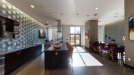 The DelRay Club is a thoughtfully designed, single-floor amenity space that blends contemporary architecture with eclectic, curated interiors. Guests are welcomed through a striking glass-enclosed entry vestibule that opens into a spacious, polished concrete-floored corridor, setting a modern and refined tone throughout.

The gourmet kitchen serves as a central showpiece, featuring dark granite island countertops with seating for multiple guests, a full suite of stainless steel appliances including a gas cooktop with a suspended range hood, and a bold decorative wall treatment that adds visual depth. Large windows flood the kitchen with natural light and provide views of an outdoor patio area.

Multiple lounge zones are distributed throughout the space, each with its own distinct character. Velvet sofas, richly upholstered armchairs in jewel tones, and a dramatic textured mosaic accent wall create intimate gathering areas. Large floor-to-ceiling windows frame outdoor views and allow sunlight to pour in.

A dedicated game room houses full-sized poker tables, moody deep-red walls, stylish pendant lighting, and card-themed artwork, offering a private and atmospheric setting for entertainment. Throughout the corridors, original artwork, sculptural installations, and curated décor reflect a strong design sensibility, making the DelRay Club a visually dynamic and functional communal destination.
