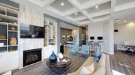 The Resident Lounge is a thoughtfully designed communal space that seamlessly blends comfort, functionality, and modern style. The lounge is anchored by a sleek fireplace framed by a built-in shelving unit finished in crisp white, providing both a decorative focal point and practical display space. Overhead, an elegant coffered ceiling adds architectural depth and visual interest to the main seating area, which is furnished with a plush neutral sofa, a round wooden coffee table, and patterned accent chairs in rich teal tones.

Flowing naturally from the main lounge is a café-inspired bar area, defined by a slate-gray accent wall and illuminated by pendant lighting. Bar-height seating lines the counter, creating an inviting spot for casual dining or socializing. Warm wood-look flooring runs throughout, grounding the space with a cohesive, contemporary aesthetic.

A dedicated workstation area along one wall features multiple computer monitors and bar-height desks, catering to residents who need a productive workspace outside their home. Framed artwork and curated décor accessories are distributed throughout, adding personality and a polished finish. The overall ambiance is welcoming, versatile, and well-appointed, making this lounge an ideal gathering place for both relaxation and productivity.