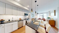 Located at 4700 Hampden Lane in the heart of Bethesda, MD, this well-appointed two-bedroom, two-bathroom residence offers a thoughtfully designed single-level layout with approximately 930 square feet of comfortable living space. Warm hardwood floors flow throughout, lending a cohesive and inviting character to every room.

The open-concept kitchen is a standout feature, equipped with full stainless steel appliances including a gas range, dishwasher, and large refrigerator. Crisp white cabinetry extends to the ceiling, complemented by a classic subway tile backsplash and dark countertops. A kitchen island with seating for two and stylish pendant lighting makes the space equally functional and visually striking.

The living room offers generous natural light through large windows, framing urban views of Bethesda's skyline. The bright, neutral palette creates a calm and welcoming atmosphere throughout.

Both bedrooms are comfortably sized, with the primary bedroom featuring multiple windows that fill the room with natural light and offer city views. Each room benefits from dedicated closet space.

The two bathrooms are finished with classic black-and-white mosaic tile floors. One bathroom features a soaking tub with subway tile surround, while the other includes a marble-topped vanity, both maintaining a clean, timeless aesthetic throughout.