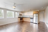 This well-designed two-bedroom, two-bathroom residence at 1608 S Dearborn St in Seattle's Beacon Hill neighborhood offers a clean, contemporary aesthetic across a single floor. The open-concept kitchen and living area serves as the heart of the home, featuring an L-shaped kitchen with two-tone cabinetry—light wood lower cabinets paired with high-gloss white uppers—dark countertops, and a full suite of stainless steel appliances including a range, microwave, dishwasher, and refrigerator. Track lighting illuminates the kitchen, while a ceiling fan adds comfort to the living area, which benefits from multiple windows that bring in natural light and views of surrounding greenery. Wood-style plank flooring runs throughout the entire residence, lending warmth and continuity. A bright hallway connects the bedrooms and bathrooms, with ample closet storage provided by four closets total. The primary bedroom is generously proportioned and includes dual sliding-door closets and natural light from dual windows. The second bedroom is cozy and bright with its own window. Both bathrooms feature wood-toned vanities with dark countertops and wood-style flooring. One bathroom conveniently includes an in-unit stacked washer and dryer. The overall ambiance is clean, modern, and move-in ready.