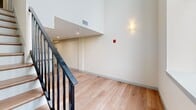 This two-bedroom, two-bathroom unit at 160 Seabury St in Fall River, Massachusetts is spread across two floors, offering a well-organized layout with a functional hallway and staircase connecting the levels. The main floor provides the larger share of the living space, while the upper floor houses additional rooms in a more intimate configuration.

Throughout the unit, light-toned hardwood flooring creates a warm, cohesive aesthetic. The staircase features a sleek black metal railing, and the upper landing benefits from dramatic ceiling height, enhanced by a striking arched window that allows natural light to filter through. Wall sconces provide ambient lighting along the hallway.

Both bedrooms are finished with the same hardwood flooring and neutral walls. One bedroom includes a built-in closet with sliding doors, while the primary bedroom features a bi-fold closet. The rooms are compact yet efficiently designed.

The two bathrooms share a consistent design language, each featuring hexagonal white tile flooring and gray vanities topped with granite counters. One bathroom includes a stand-up shower with a chrome-framed glass door and a grab bar, while the other offers a full toilet and vanity setup. Clean lines and neutral tones give both bathrooms a fresh, modern feel throughout.