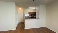 Located in Grand Prairie, Texas, this single-story residence offers a practical and well-appointed interior designed for comfortable everyday living. The open-concept layout seamlessly connects the kitchen and living areas, creating a spacious and inviting atmosphere. The kitchen is equipped with stainless steel refrigerator, a black range, and a built-in microwave, all complemented by rich dark wood cabinetry and granite-style countertops. A peninsula-style breakfast bar provides additional prep and dining space while reinforcing the open flow of the floor plan. Rich, dark wood-style flooring runs throughout the main living areas, adding warmth and a modern aesthetic. The neutral, light-toned walls create a bright and airy feel that enhances the sense of space. Recessed and flush-mount lighting ensures consistent illumination throughout. An entryway near the kitchen provides easy access to additional rooms, with white paneled doors adding a clean, classic touch. Overall, this space strikes a balance between modern functionality and comfortable design, making it a welcoming and practical home in the Grand Prairie area.