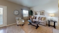 This single-floor residence offers a thoughtfully designed layout with a cohesive, neutral aesthetic throughout. The kitchen is a standout space, showcasing dark cabinetry with sleek hardware contrasted against crisp white countertops and light wood-style flooring. Stainless steel appliances, including a refrigerator, range, microwave, and dishwasher, provide a modern touch, while pendant lighting and an island with bar seating add both function and style.

The living room is warm and inviting, featuring carpet flooring, a window that brings in natural light, and ample space for comfortable furnishings. Adjacent bedrooms continue the carpeted, light-toned design; the primary bedroom includes a ceiling fan and a closet with panel doors, while a secondary bedroom offers a cozy, versatile space.

The bathroom is cleanly finished with a tub-shower combination, a dark-toned vanity with a light countertop, and tile flooring. A dedicated laundry closet houses a full-size side-by-side washer and dryer with overhead wire shelving for storage. A separate utility area accommodates the water heater, completing the home's functional footprint.