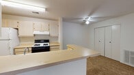 This single-floor residence offers a practical and comfortable layout designed for everyday living. The kitchen is a standout feature, presenting two distinct configurations across the unit — one with an open, peninsula-style breakfast bar that connects seamlessly to the carpeted living area, complete with light wood cabinetry, a gas range, and overhead ventilation. A separate galley kitchen configuration offers ample counter space, light wood cabinetry, a gas range, a full-size refrigerator, and tile flooring, providing efficient workflow for cooking and meal preparation. The living and bedroom areas are finished with warm, neutral-toned carpet throughout, creating a cohesive and inviting atmosphere. A ceiling fan with a light fixture provides comfort and airflow to the main living space. The hallway connects the rooms with ease, lined with closet storage and wall-mounted ventilation. The full bathroom features a tub-shower combination, a vanity with light wood cabinetry, and tile flooring in a soft stone pattern. A generously sized walk-in closet with wire shelving offers abundant storage. Natural light filters into the bedrooms through vertical-blind-covered windows, adding brightness to the neutral, move-in-ready interiors.