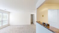 Located at 1202 Townsend Blvd in Fredericksburg, VA, this single-floor residence offers three bedrooms and two bathrooms within a thoughtfully arranged floor plan. The open living area is finished with neutral-toned carpeting and crisp white walls, creating a bright and clean atmosphere. A half-wall peninsula separates the living space from the kitchen, which features granite-style laminate countertops, a stainless steel sink, and warm wood cabinetry providing ample storage. The primary bedroom offers a comfortable footprint with carpeted floors and generous closet space behind classic double panel doors. The two additional bedrooms share a similar layout with soft carpeting and neutral walls, making them well-suited for various uses. The two bathrooms include chrome hardware and towel bars; one features a full tub-shower combination. A dedicated laundry room houses a full-size top-loading washer and dryer with wire shelving above for additional storage. Two hallways connect the rooms efficiently throughout the unit. Natural light filters in through windows visible in the floorplan overview, contributing to the home's clean, airy feel. The overall design is functional and straightforward, ideal for those seeking a well-equipped residence in Fredericksburg.