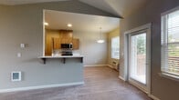 Located at 1881 Wiltsey Rd SE in Salem, Oregon, this single-floor residence offers a thoughtfully designed layout that balances functionality and comfort. The open-concept living and dining area is anchored by vaulted ceilings and large windows that invite abundant natural light, creating an airy and welcoming atmosphere. A sliding glass door provides direct access to the outdoors, further enhancing the sense of openness.

The kitchen is a standout feature, equipped with stainless steel appliances including a refrigerator, electric range, and over-the-range microwave. Warm-toned wood cabinetry, white countertops, and a peninsula with bar seating define the space, making it both practical and visually appealing. Wood-style hard flooring runs throughout the main living areas, adding warmth and durability.

The bedrooms offer a comfortable retreat, with one featuring vaulted ceilings, wood-style flooring, and a bright window with outdoor views, while another is finished with plush carpeting and natural light from a well-placed window. The bathroom includes a clean, white tub and shower surround. Neutral gray and taupe tones are used consistently throughout the residence, lending a cohesive and modern aesthetic to every room.