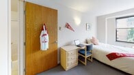Located at 155 Dryden Rd in Ithaca, NY, this single-floor unit is well-suited for student living in close proximity to Cornell University. The layout is compact and efficiently organized, encompassing a bedroom, kitchen, and full bathroom.

The bedroom is carpeted and furnished with a bed, a three-drawer dresser, an open shelving unit, and a dedicated study area complete with a desk and chair — providing all the essentials for both rest and academic work. A wall-mounted light fixture adds ambient lighting, and a large window allows natural light to fill the room while offering views of surrounding greenery.

The kitchen is thoughtfully equipped with white cabinetry offering generous storage, a light-toned countertop, an electric range, a microwave, and a single-basin sink. The layout supports efficient meal preparation within a modest footprint.

The bathroom features a clean, functional design with light-toned flooring, a combination tub and shower enclosed by sliding glass doors, a single vanity with an integrated sink, and mirrored medicine cabinets that enhance the sense of space. The overall aesthetic throughout the unit is neutral and understated, with white walls and light-colored finishes creating a bright, livable environment.
