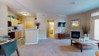 This well-appointed single-floor residence offers a thoughtfully designed layout that balances comfort and functionality throughout. The open living area serves as the heart of the home, featuring plush wall-to-wall carpeting, a classic fireplace with a decorative mantel, and a wall-mounted television setup. A large glass door leads to a private balcony, flooding the space with natural light and offering pleasant outdoor views. A half-wall partition gracefully separates the living area from the adjacent kitchen zone, adding architectural definition without sacrificing openness.

The galley-style kitchen is efficiently arranged with light wood cabinetry lining both sides, providing generous storage and counter space. White appliances, including a range and refrigerator, are complemented by a double sink and dishwasher.

The primary bedroom is generously sized, featuring soft carpeting, dual windows that invite natural light, and a closet for ample storage. The second bedroom mirrors this comfortable layout with its own window and closet access.

Two full bathrooms serve the residence, each equipped with a vanity, mirror, and a tub-shower combination. Neutral tones and tile flooring carry a clean, practical aesthetic throughout both spaces. Overall, the residence presents a warm, livable ambiance with consistent finishes and a practical floor plan.