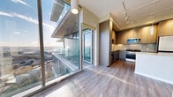 This 810-square-foot high-rise residence on Yesler Way in Seattle delivers a sleek, modern design across a single floor. The open-concept living room features light hardwood flooring, floor-to-ceiling windows, and expansive city and mountain views, flooding the space with natural light. A pendant light fixture adds a contemporary accent to the airy layout.

The kitchen is well-appointed with stainless steel appliances, including a range, microwave, and refrigerator, complemented by flat-front cabinetry in warm wood tones, a stone tile backsplash, granite countertops, and a central island with pendant lighting. Light hardwood floors and track lighting complete the modern aesthetic.

The 130-square-foot primary bedroom features plush carpeting, large windows with sweeping city views, and access to two closets—one a walk-in with built-in shelving systems offering organized storage.

Three bathrooms are finished with large-format tile flooring, granite-topped wood vanities, backlit mirrors, and polished chrome fixtures. One bathroom includes a soaking tub, while another features a glass-enclosed shower, delivering a refined, spa-like atmosphere throughout.