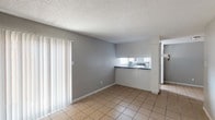 This single-floor unit offers 2 bedrooms and 1 bathroom, designed with a straightforward and functional layout. The living and dining area is finished with light-toned ceramic tile flooring and neutral gray walls, creating a clean and cohesive look. A large sliding glass door fitted with vertical blinds allows natural light to fill the space and provides easy access to the outdoors. The kitchen features a pass-through counter that opens to the living area, white cabinetry, dark laminate countertops, a double stainless steel sink, and a window above the counter that brings in additional natural light. Both bedrooms are finished with tile flooring, neutral gray walls, and textured ceilings, with ceiling fans providing ventilation and overhead lighting. One bedroom features darker tile flooring, adding a subtle contrast to the rest of the unit. Throughout the space, white baseboards provide a clean finish against the gray walls. The textured popcorn ceilings are consistent across all rooms, contributing to the unit's practical, no-frills character. Overall, the space is bright, easy to maintain, and offers a functional floor plan suited for everyday living.