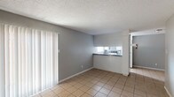 This single-floor unit offers 2 bedrooms and 1 bathroom, designed with a straightforward and functional layout. The living and dining area is finished with light-toned ceramic tile flooring and neutral gray walls, creating a clean and cohesive look. A large sliding glass door fitted with vertical blinds allows natural light to fill the space and provides easy access to the outdoors. The kitchen features a pass-through counter that opens to the living area, white cabinetry, dark laminate countertops, a double stainless steel sink, and a window above the counter that brings in additional natural light. Both bedrooms are finished with tile flooring, neutral gray walls, and textured ceilings, with ceiling fans providing ventilation and overhead lighting. One bedroom features darker tile flooring, adding a subtle contrast to the rest of the unit. Throughout the space, white baseboards provide a clean finish against the gray walls. The textured popcorn ceilings are consistent across all rooms, contributing to the unit's practical, no-frills character. Overall, the space is bright, easy to maintain, and offers a functional floor plan suited for everyday living.