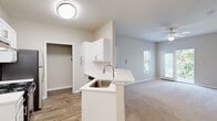 Located at 1560 Wimbledon Dr in Greenville, NC, this single-floor residence presents a bright, clean aesthetic defined by neutral tones and practical finishes throughout. The open-concept layout connects the kitchen directly to the living area, creating a cohesive and functional common space. The kitchen is well-appointed with white shaker-style cabinetry, a classic subway tile backsplash, light countertops, stainless steel appliances including a refrigerator and range, a built-in dishwasher, and a peninsula with a single-basin sink that overlooks the living area. A chandelier adds a refined touch above the adjacent dining space, which features wood-look flooring that extends through the kitchen.

The living area is generously proportioned, finished with plush neutral carpeting, a ceiling fan, and windows that invite natural light and outdoor views of surrounding greenery. A front entry door with panel detailing anchors the space. The bedrooms continue the carpeted flooring and ceiling fan theme, with one room offering a private walk-in closet with built-in shelving and another featuring a glass sliding door leading to an outdoor area with wooded views. The bathroom is finished with white cabinetry, a wide vanity mirror, a tub-shower combination with tile surround, chrome fixtures, and wood-look flooring, maintaining the home's cohesive, clean design throughout.