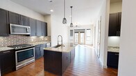 Located in Southside Place, TX, this well-appointed one-bedroom, one-bathroom residence offers a thoughtfully designed open floor plan. The kitchen serves as the heart of the home, showcasing dark cabinetry, a striking brick-tile backsplash, stainless steel appliances — including a refrigerator, range, microwave, and dishwasher — and a large central island topped with light granite countertops. Industrial-style geometric pendant lights hang above the island, adding a modern touch. Rich hardwood flooring flows throughout the main living areas, enhancing the warm, contemporary aesthetic. The living room is bright and airy, bathed in natural light from large windows and French doors that open onto a private balcony, offering outdoor views. A ceiling fan provides additional comfort. The bedroom is carpeted for coziness, features its own ceiling fan and a large window for natural light, and includes access to a dedicated closet. The bathroom continues the design language of the home with dark cabinetry, granite countertops, a well-lit vanity mirror, and clean tile flooring. Throughout the space, a consistent palette of neutral tones, quality finishes, and modern fixtures creates a cohesive and functional living environment.