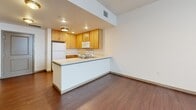 Located at 3401 S Broadway in Englewood, Colorado, this one-bedroom, one-bathroom residence offers a thoughtfully designed single-floor layout. The kitchen is a standout feature, showcasing warm honey-toned wood cabinetry extending to the ceiling, white appliances including a full-size refrigerator, electric range, and built-in microwave, all set atop rich wood-style flooring. A peninsula counter with a light-colored surface opens the kitchen toward the living area, creating a connected, functional flow between spaces. Recessed lighting illuminates both areas efficiently. The living space offers a clean, open canvas with the same wood-style flooring continuing throughout. The bedroom is generously sized, featuring plush wall-to-wall carpeting, a large window fitted with vertical blinds that invite natural light, and direct access to a spacious walk-in closet complete with wire shelving and carpet flooring. The full bathroom maintains a cohesive aesthetic with wood-look tile flooring, a full-size soaking tub with a tiled surround and shower, a toilet, and matching wood cabinetry for storage. The overall ambiance is clean, neutral, and move-in ready, offering a practical and comfortable living environment in a convenient Englewood location.
