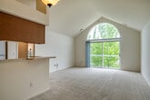 This single-floor residence offers a thoughtfully designed layout that balances comfort and functionality. The living area immediately impresses with its dramatic vaulted ceiling and a striking arched window paired with full-height sliding glass doors that open onto a private balcony, flooding the space with natural light and providing lush tree-lined views. Soft, neutral carpet extends throughout the living and bedroom areas, contributing to a warm and inviting ambiance.

The kitchen is open to the living space and features warm oak cabinetry that extends to the vaulted ceiling, making excellent use of vertical space. A peninsula with a light stone-toned countertop and an integrated sink provides additional workspace and a natural transition between the kitchen and the living area. Pendant lighting accents the space, and tile flooring adds a practical, easy-to-maintain surface underfoot.

The bedrooms are generously proportioned, each with plush carpet and large windows that bring in ample daylight and offer pleasant views of the surrounding neighborhood and greenery. The two full bathrooms are consistent in their design, each featuring warm oak vanity cabinetry, stone-toned countertops, a wide vanity mirror with overhead lighting, and a full tub and shower combination with chrome fixtures and tile flooring.