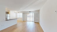 This single-floor unit offers a clean, functional layout designed to maximize comfort and usability. The open-concept living and dining area is finished with light hardwood-style flooring that runs throughout, creating a cohesive and airy feel. Large sliding glass doors and multiple windows allow abundant natural light to fill the space, while providing views of the surrounding exterior. A half-wall peninsula separates the living area from the kitchen, which features stainless steel appliances including a refrigerator, range, and microwave, complemented by gray cabinetry and dark countertops. The kitchen also provides direct access to an entry door, adding convenience. The bedrooms are carpeted for warmth and comfort, each benefiting from natural light through window treatments. At least one bedroom includes a built-in closet with louvered doors, offering practical storage. The bathroom is finished in a clean, neutral palette, featuring a white vanity with under-sink storage, a mirror, and a combination tub and shower. Throughout the unit, white walls and consistent trim work contribute to a bright, well-maintained atmosphere suited for everyday living.