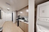 Located at 1743 Butler Avenue in the heart of West Los Angeles, this efficiently designed one-bedroom, three-bathroom unit offers a remarkably functional layout. Light wood flooring runs throughout, complemented by a clean, neutral palette that enhances the sense of openness.

The hallway serves as the central spine of the unit, connecting all rooms while displaying modern décor accents. The galley-style kitchen is fitted with warm wood cabinetry extending to the ceiling, stainless steel appliances including a gas range and dishwasher, and a white countertop with an undermount sink. A stacked washer and dryer unit is conveniently integrated nearby.

The bedroom makes smart use of its footprint with a built-in Murphy bed system paired with integrated storage cabinetry. Multiple windows and a sliding glass door flood the room with natural light and provide views of surrounding greenery, while a wall-mounted TV adds a practical amenity.

Three bathrooms serve the unit, each finished with light wood-tone cabinetry, clean tile work, and modern fixtures. One bathroom features a glass-enclosed walk-in shower with floor-to-ceiling tile and a wall-mounted cabinet, while others include vanities with mirrored medicine cabinets and tall storage towers. The overall design prioritizes intelligent use of space without sacrificing modern comfort or style.