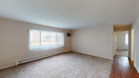 Located at 619 Gundersen Dr in Carol Stream, Illinois, this single-floor unit offers a practical and comfortable layout across several well-defined living spaces. The living room is generously sized, featuring wall-to-wall carpeting, neutral-toned walls, a large picture window dressed with vertical blinds that allows ample natural light, a baseboard heating system, and a wall-mounted air conditioning unit for year-round climate control. An open passageway connects the living room to a dining area, which transitions into the kitchen. The kitchen is equipped with warm-toned wooden cabinetry, granite-style countertops, a double sink, a gas range, a dishwasher, and a refrigerator, all set atop durable hardwood-style flooring. A ceiling fan overhead adds to the functionality of this space. The bedroom features plush carpeting, neutral walls, and a built-in closet with a hanging rod for ample storage, along with a ceiling light fixture. The full bathroom includes a tub-shower combination with tile surround, a toilet, a single vanity with under-sink cabinetry, and warm hardwood-style flooring. Clean white six-panel doors are featured throughout, contributing to a cohesive and tidy aesthetic across the unit.
